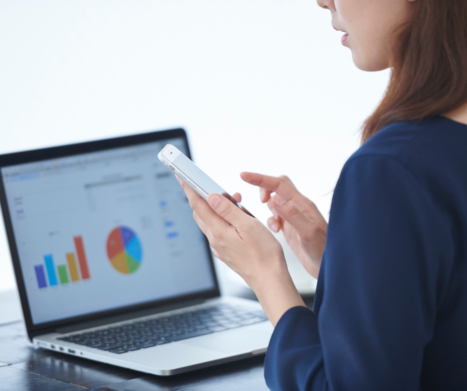 A business professional reviewing analytics on a smartphone while working with charts and graphs on a laptop screen, representing digital transformation, data-driven decision-making, and integrated marketing intelligence in modern enterprises.