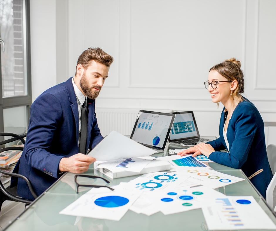 Two business professionals analysing charts and digital dashboards in a modern office, representing collaboration, data-driven decision-making, and strategic planning powered by analytics and enterprise intelligence.