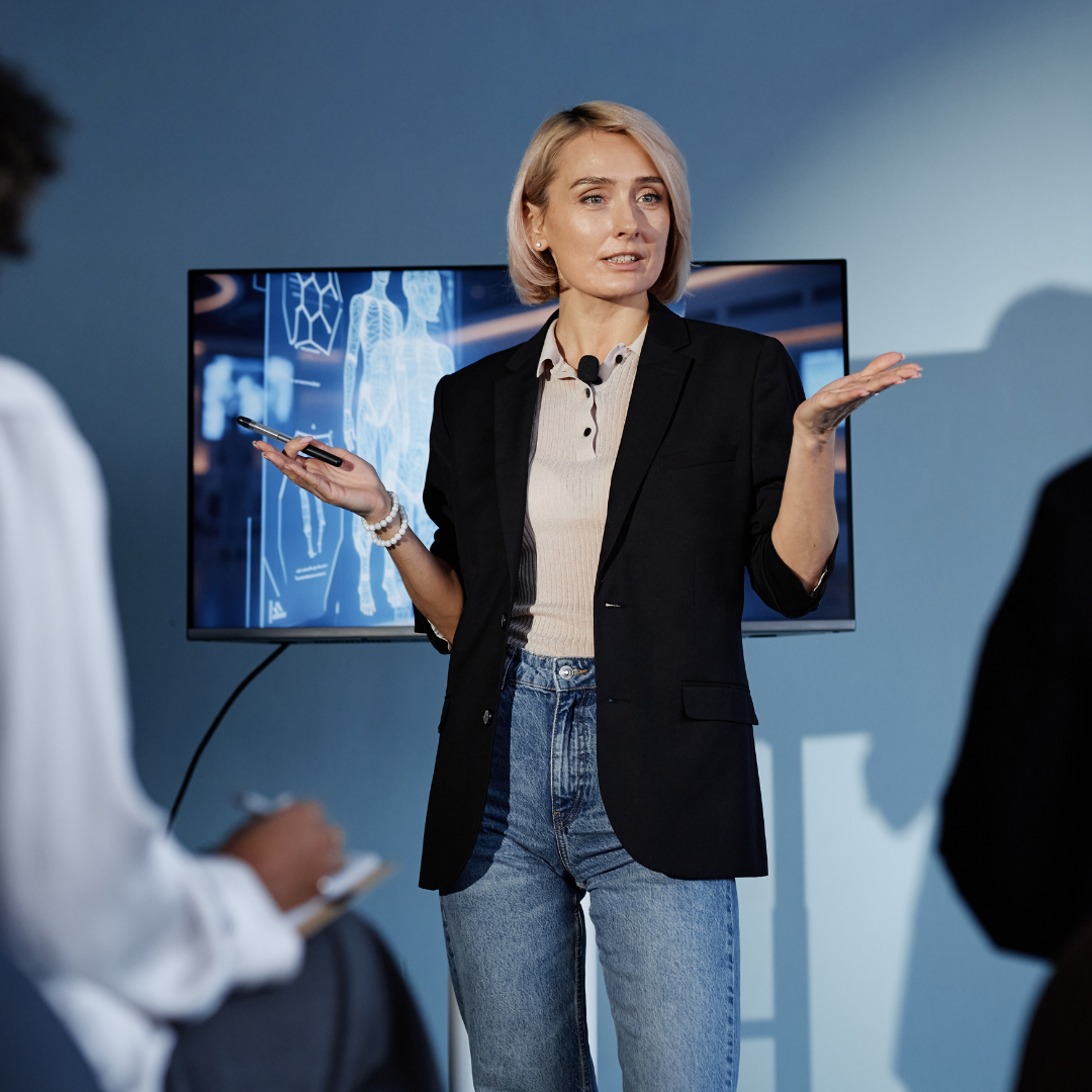 blog feature image (updated) (1) Business professional presenting in front of a screen with data visuals during a meeting or training session.
